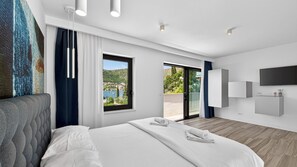 A modern hotel room with a large bed, a TV, a balcony with a scenic view, and a painting on the wall.