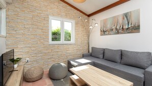 Una sala de estar moderna con una pared de piedra, un sofá gris, una mesa de centro de madera, un taburete redondo tejido y un cuadro de veleros.