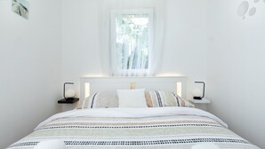 Un dormitorio minimalista con cama, mesitas de noche y una ventana con cortinas translúcidas.
