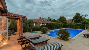 Un jardin avec une piscine, des chaises longues et une maison en pierre.