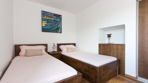 Une chambre avec deux lits, une table de chevet, une lampe, un tableau et une armoire en bois.