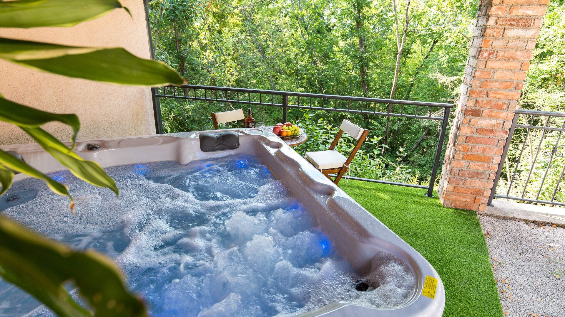 A hot tub with a table and chairs, surrounded by greenery and a brick wall.