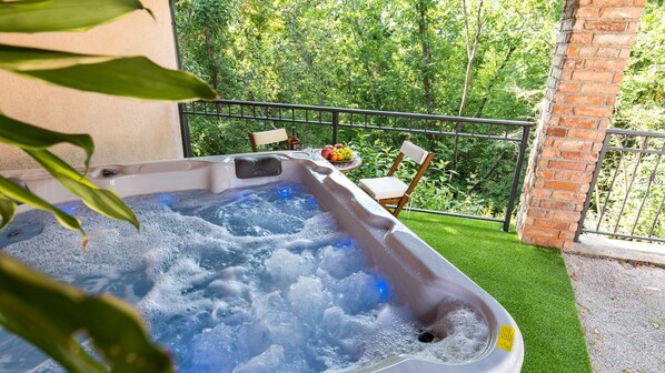Un jacuzzi con una mesa y sillas, rodeado de follaje y un muro de ladrillo.