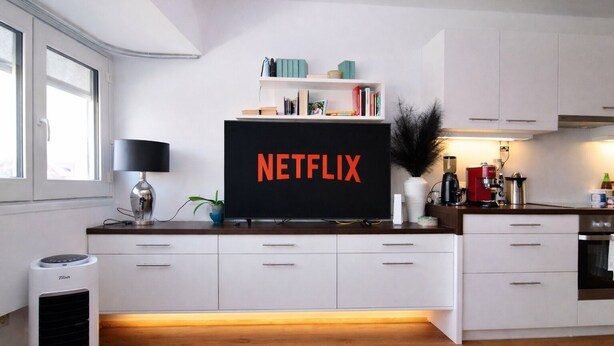 A modern kitchen with a large flat-screen TV displaying the Netflix logo, white cabinetry, a coffee machine, and a built-in air purifier.