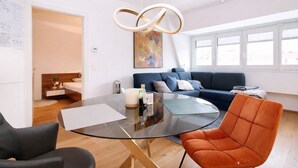 A modern living room with a glass coffee table, a blue sofa, and an orange chair.