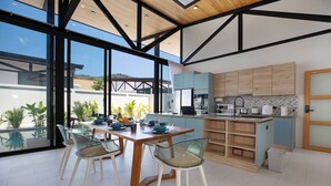 A modern kitchen with a large island, glass dining table, and chairs. - New 17m Eco Pool Villa Sunset Garden 12 (Rawai)