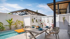 An outdoor dining area with a pool, wooden table, wicker chairs, and potted plants. - New 17m Eco Pool Villa Sunset Garden 12 (Rawai)
