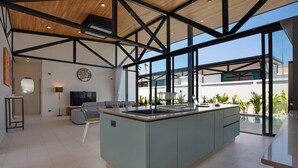 A spacious kitchen with a large island, modern appliances, and a view of a swimming pool. - New 17m Eco Pool Villa Sunset Garden 12 (Rawai)