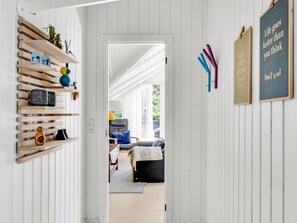 A hallway with a wooden shelf, a door leading to a living room, and motivational wall art.
