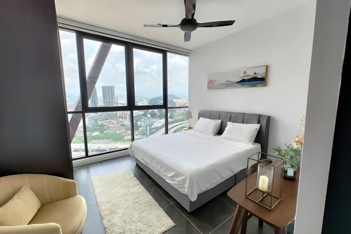 A bedroom with a large window, a bed, a ceiling fan, and a nightstand with a candle.
