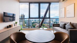 A modern office space with a large window offering a city view, a flat-screen TV, a round table, and a sofa. - Scarletz Suites KLCC by Purple Orchid (Kuala Lumpur)
