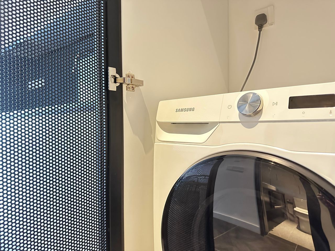 Een voor aanzicht van een Samsung wasmachine met bedieningspaneel en een aangesloten stroomkabel.