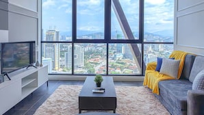 A modern living room with a large window, a flat-screen TV, a coffee table, and a sofa with a view of the city. - Scarletz Suites KLCC by Purple Orchid (Kuala Lumpur)