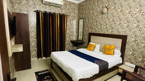A hotel room with a bed, a ceiling fan, a mirror, a nightstand, and a TV. - Hotel Taj Royale (Agra)