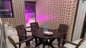 A dining area with a round table and six chairs, a water bottle, and a plate with food. - Hotel Taj Royale (Agra)