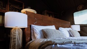 A neatly made bed with white linens and a wooden headboard, accompanied by two bedside lamps with woven bases. - Munga Plains (Kachikau)