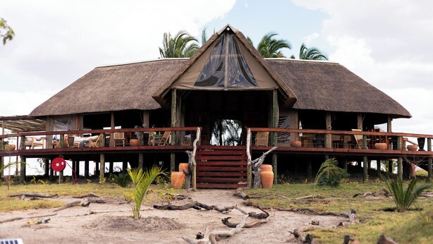 A thatched-roof building with a wooden deck and a central staircase leading to an open entrance. - Munga Plains (Kachikau)