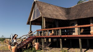 A rustic building with a thatched roof, wooden beams, and a wooden deck. - Munga Plains (Kachikau)