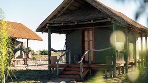 A rustic cabin with a thatched roof, wooden porch, and a hammock. - Munga Plains (Kachikau)
