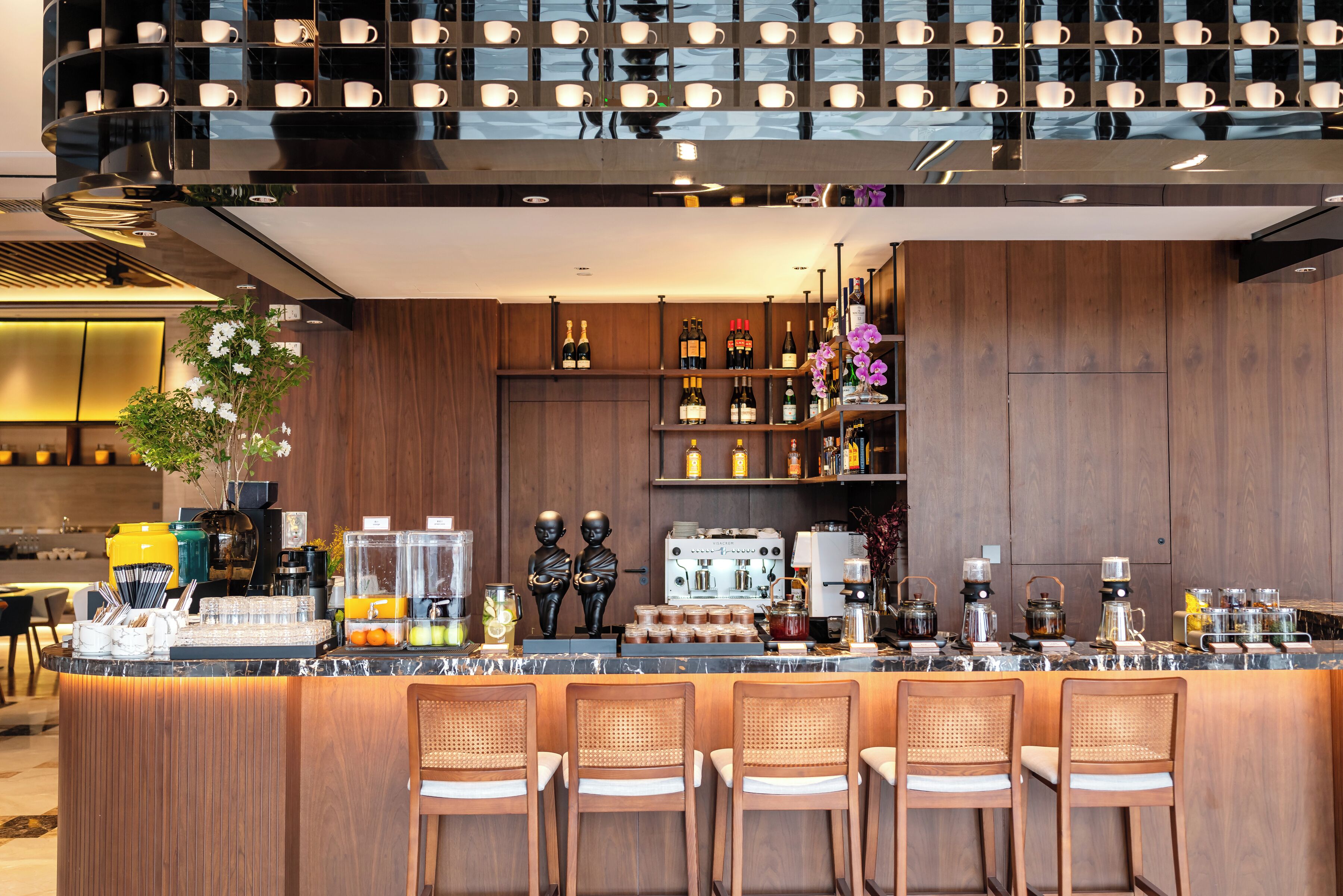 Un espace bar moderne avec des comptoirs en bois, des tabourets de bar et une grande variété de boissons et de bouteilles.