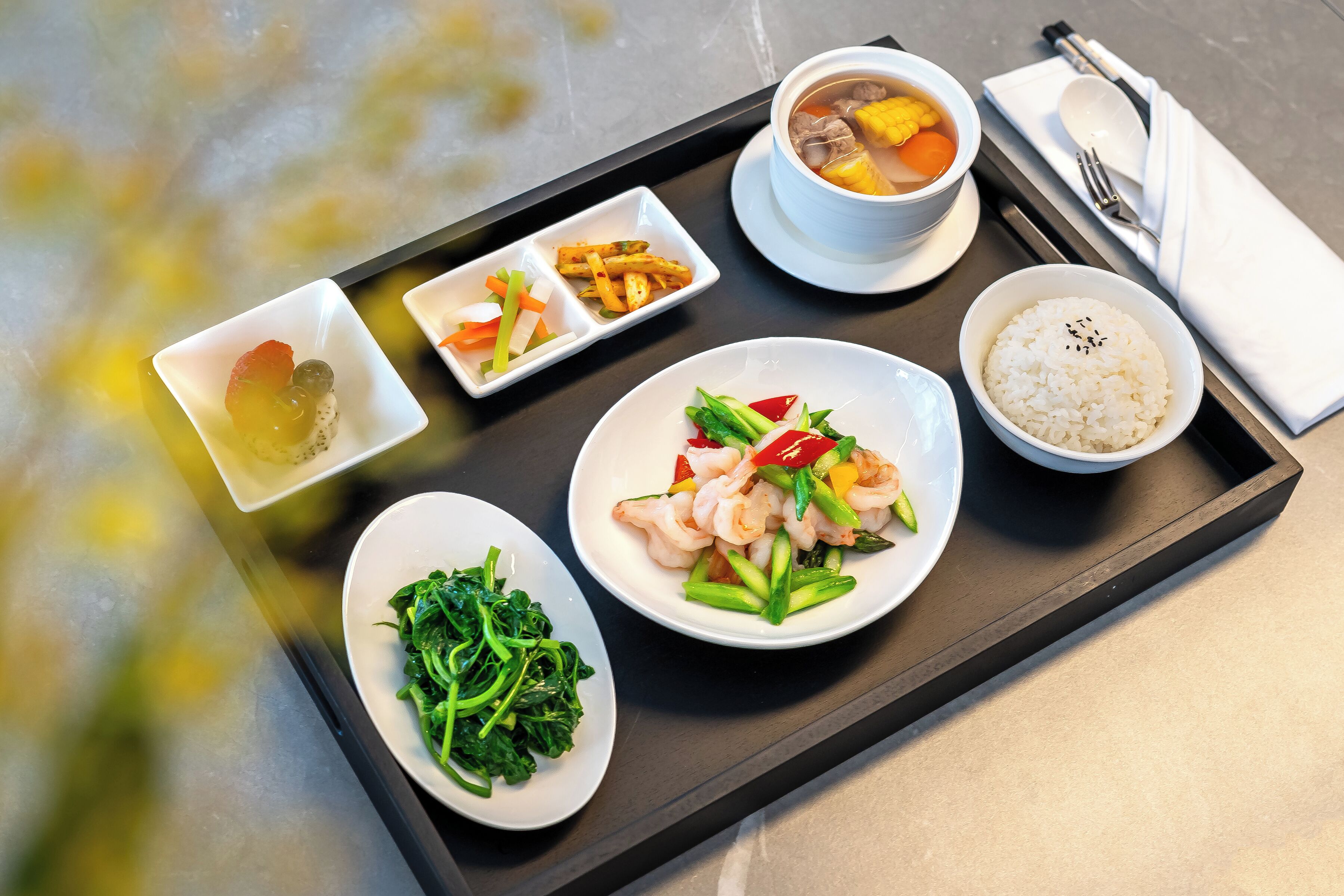 A tray with various dishes including a bowl of soup, a plate of rice, a dish with shrimp and vegetables, a plate of greens, and a small dish with pickled vegetables.