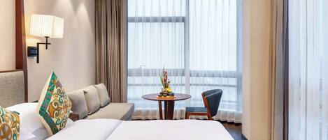 A hotel room with a large bed, a sofa, a small table with a vase, and a chair.