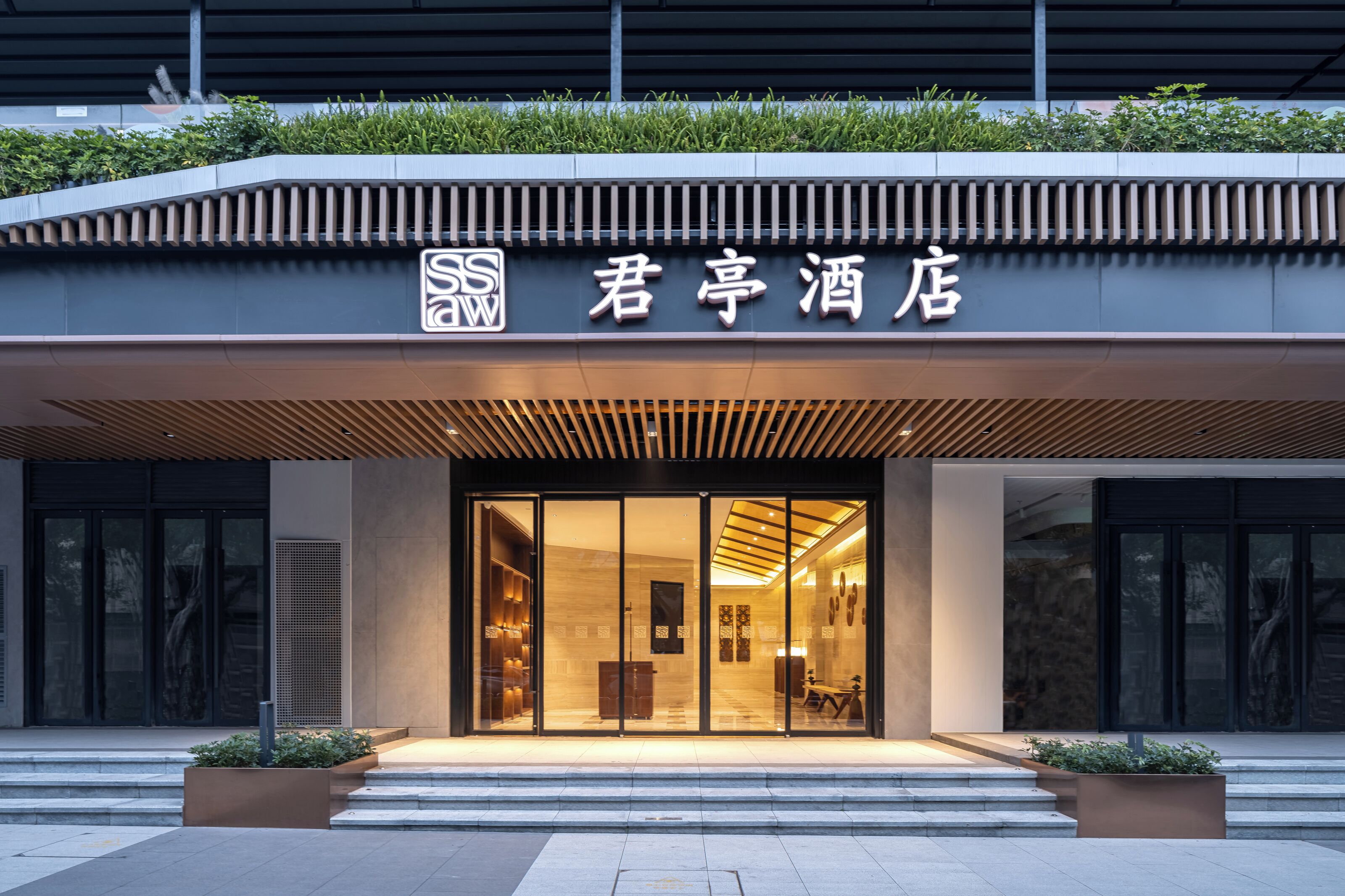 Entrada de hotel con diseño moderno, destacando un letrero con caracteres chinos y un logotipo.