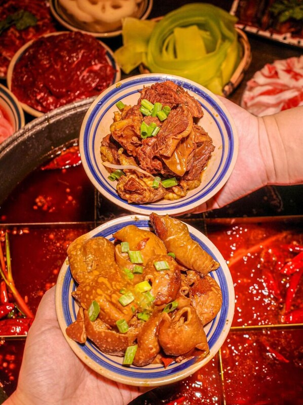 A person holding two bowls of food, one with meat and the other with seafood, with a red sauce in the background. - SSAW Boutique Hotel Swufe Chengdu (Chengdu)
