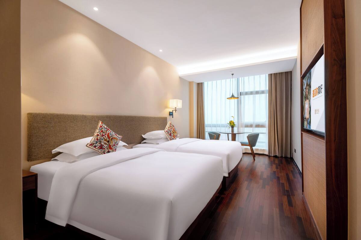 A hotel room with two beds, a small table, and a view of the outdoors.
