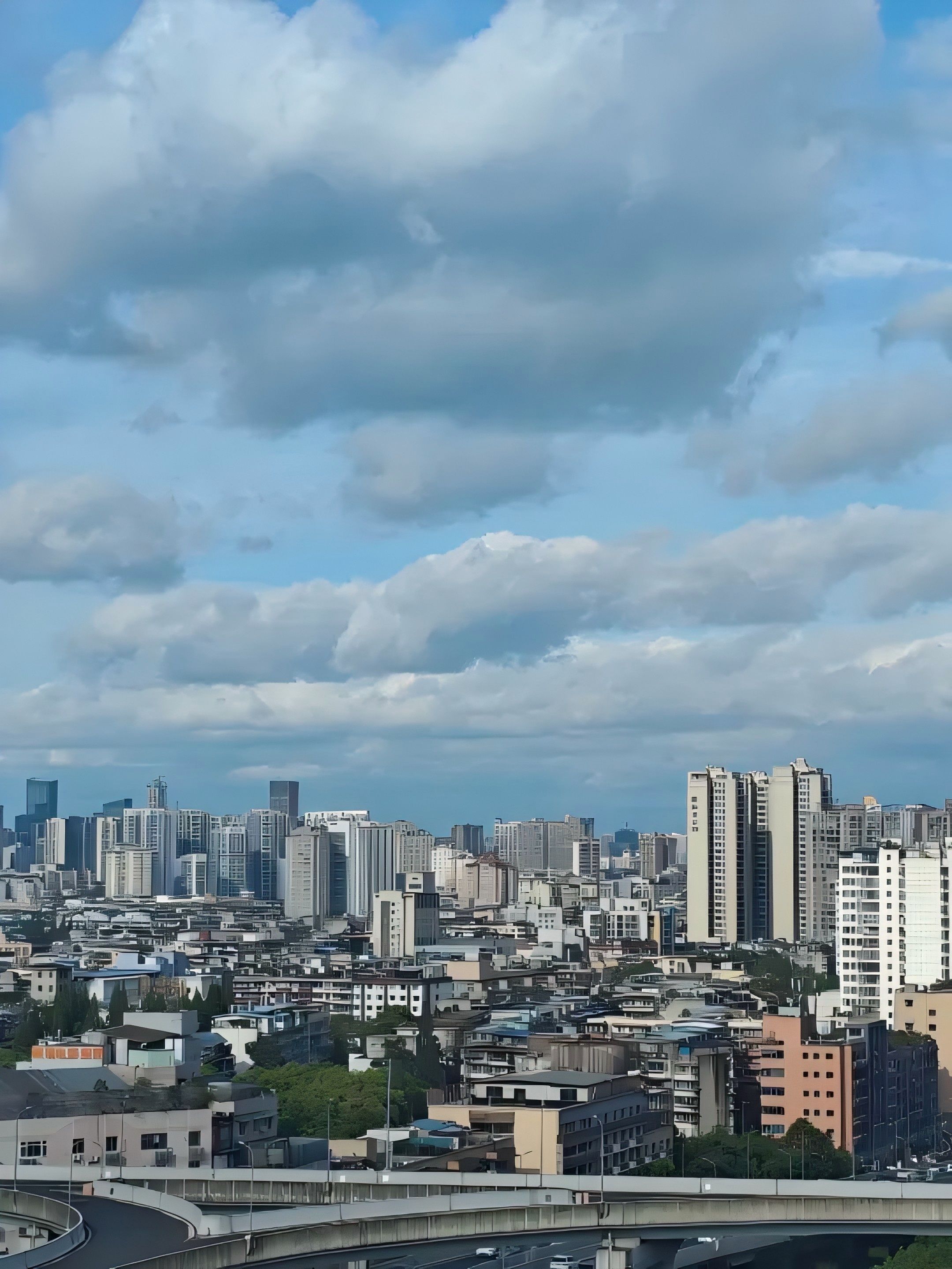 A cityscape with a variety of high-rise buildings, a curved road, and a bridge in the foreground.