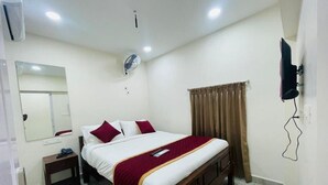 Ein Schlafzimmer mit einem großen Bett, einem Nachttisch, einem Spiegel, einem Ventilator und einem an der Wand befestigten Fernseher.