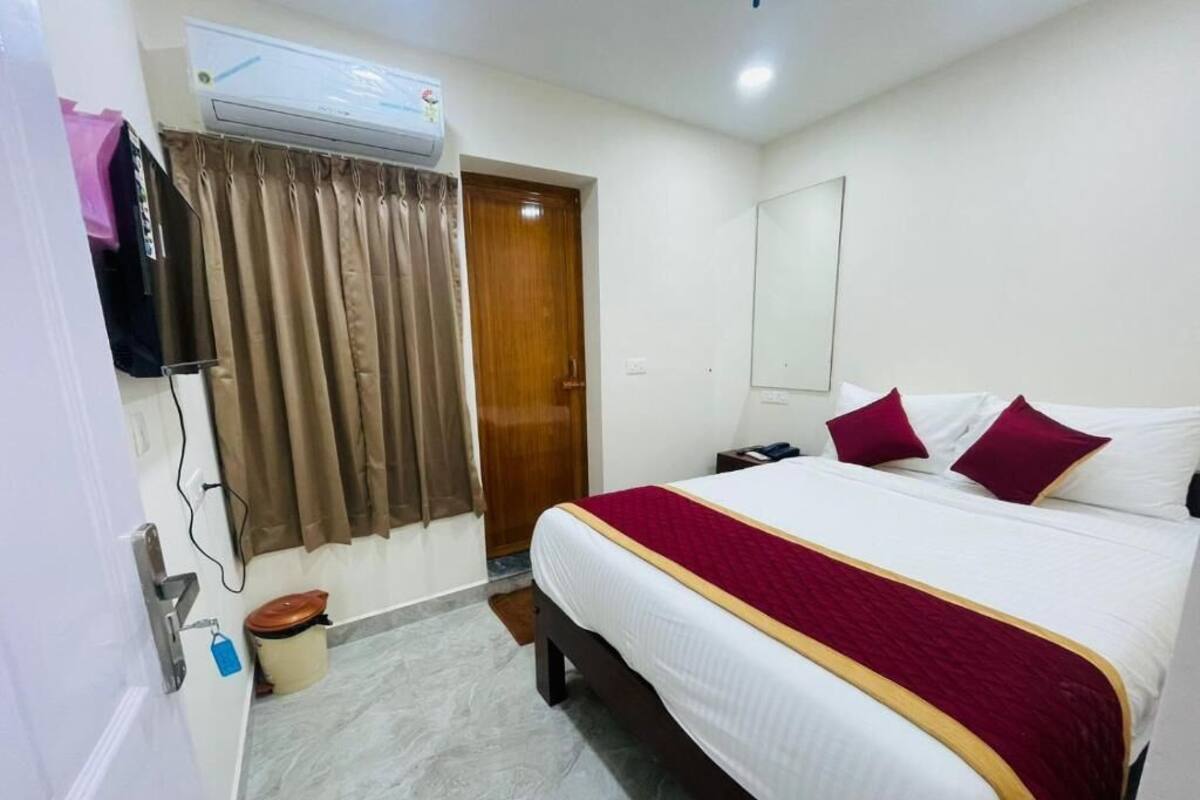 Una habitación de hotel con cama, cortinas, aire acondicionado, espejo y puerta.