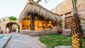 Un patio con una construcción de techo de paja, un sendero de piedra y una palmera.
