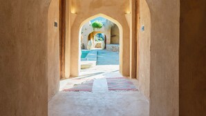 Un corredor arqueado que conduce a una zona de piscina con vistas a una estructura de piedra y una planta.