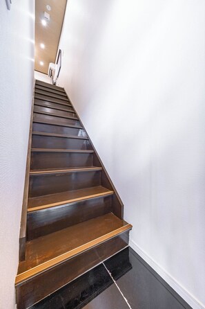 A wooden staircase with a handrail, leading to a landing with a light switch and a wall-mounted light fixture.