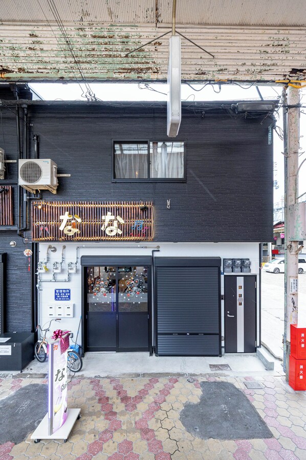 A building with a black exterior, a visible air conditioning unit, a closed black shutter door, and a bicycle parked outside.