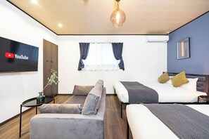 A modern hotel room with a sofa, a bed, a TV mounted on the wall, and a window with curtains.