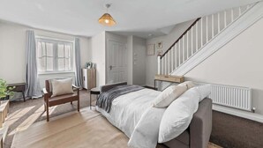 Ein Schlafzimmer mit einem Bett, einem Sessel, einem Schreibtisch, einer Heizung und einer Treppe.