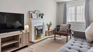 Ein modernes Wohnzimmer mit Flachbildfernseher, Kamin, Sofa und einem fenster mit Vorhängen.