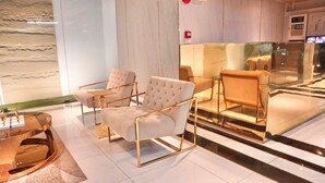 Um hall moderno com piso de mármore, divisória de vidro e área de estar com cadeiras estofadas e mesa de centro de vidro.