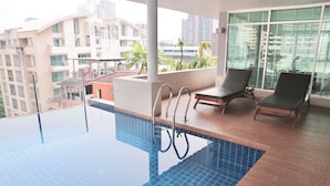 Piscina interior com azulejos azuis translúcidos, duas espreguiçadeiras e vista para edifícios próximos.