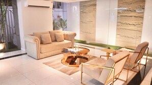 Sala de estar moderna com um sofá bege, uma mesa de centro de vidro e vista para um jardim ajardinado através de um painel de vidro.