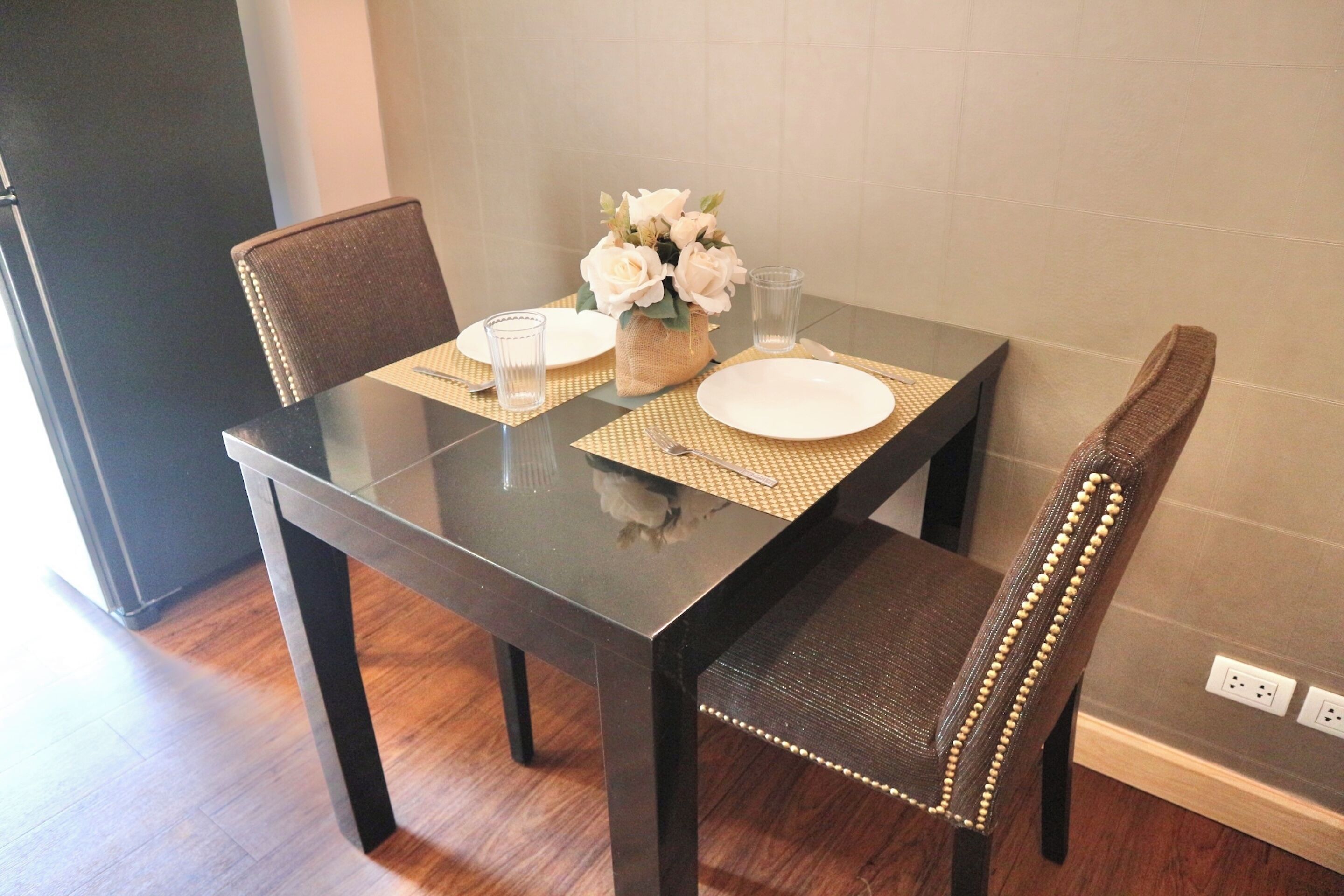 Une table à manger avec deux chaises, un vase rempli de fleurs et un verre d’eau.