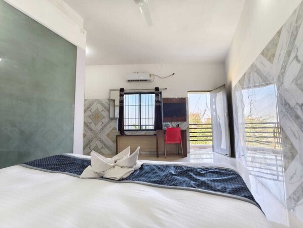 Un dormitorio con cama, escritorio, silla, televisión y balcón con vistas.