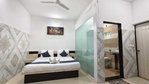 A modern hotel room with a bed, a ceiling fan, a bathroom visible through a glass partition, and a door leading to another room. - Hotel Hari Om Swimming Pool In Diu (Diu)