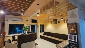 A reception area with a wooden reception desk, a seating area with patterned cushions, and a ceiling with wooden paneling and pendant lighting. - Hotel Hari Om Swimming Pool In Diu (Diu)