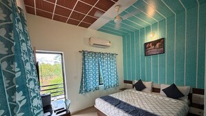 A bedroom with a bed, a desk, a chair, a window with curtains, and a ceiling fan. - Hotel Hari Om Swimming Pool In Diu (Diu)