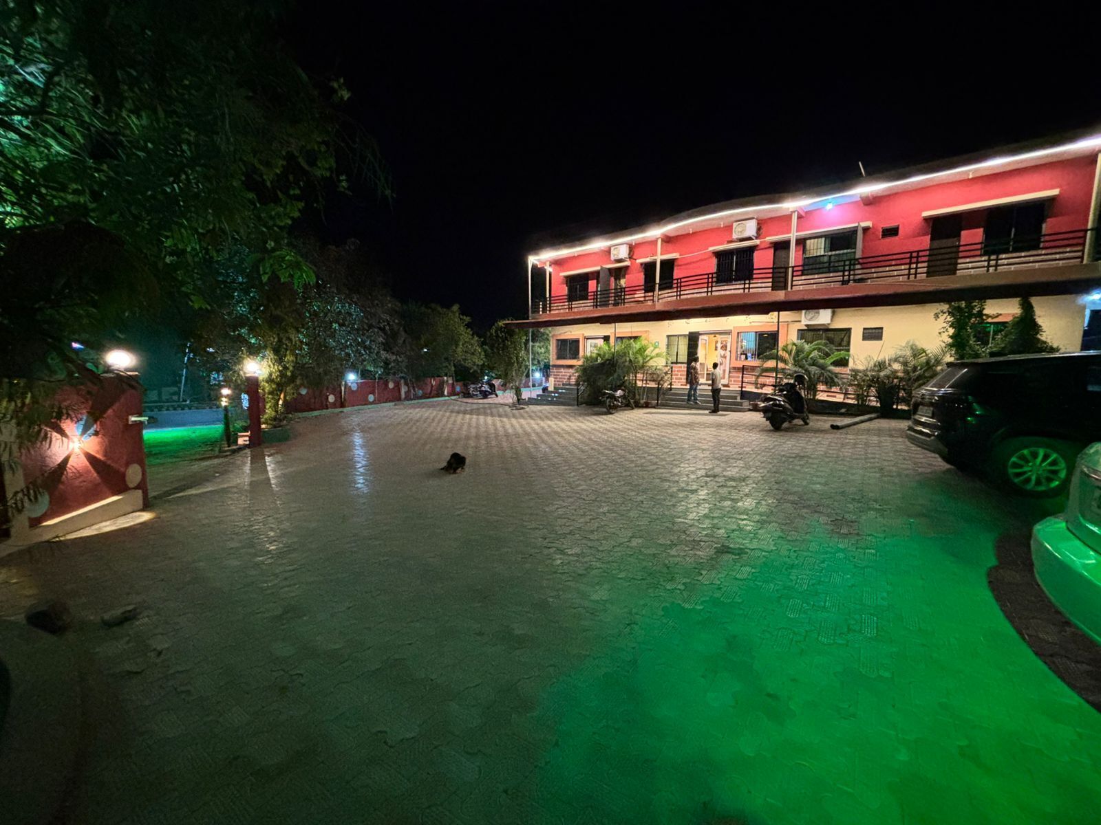 Un edificio de fachada roja, un patio empedrado y algunos vehículos estacionados.