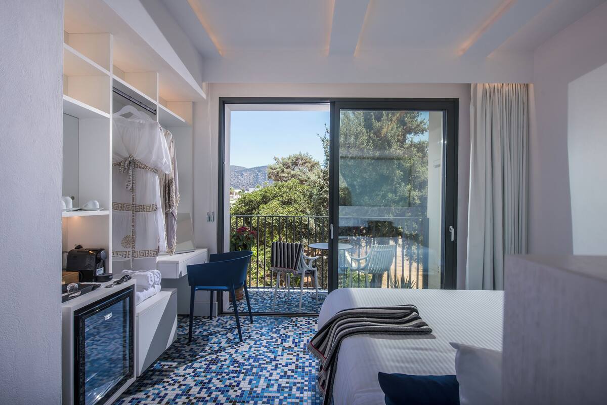 A hotel room with a bed, a seating area with chairs, a small table, a coffee machine, and a view of the outdoors.