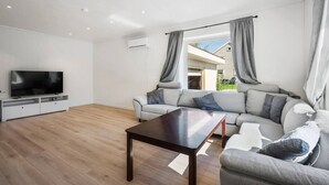 A modern living room with a flat-screen TV, a dark wooden coffee table, and a grey sectional sofa. - Large Single-family Home - Central in Voss (Voss)